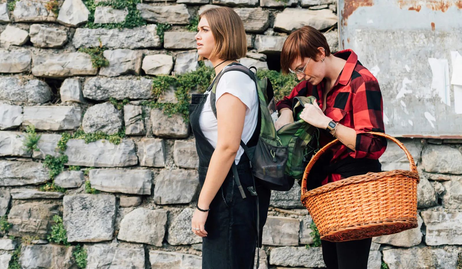 2 females working in front of a cobbled wall, one with a hand basket