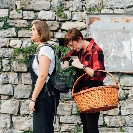 2 females working in front of a cobbled wall, one with a hand basket