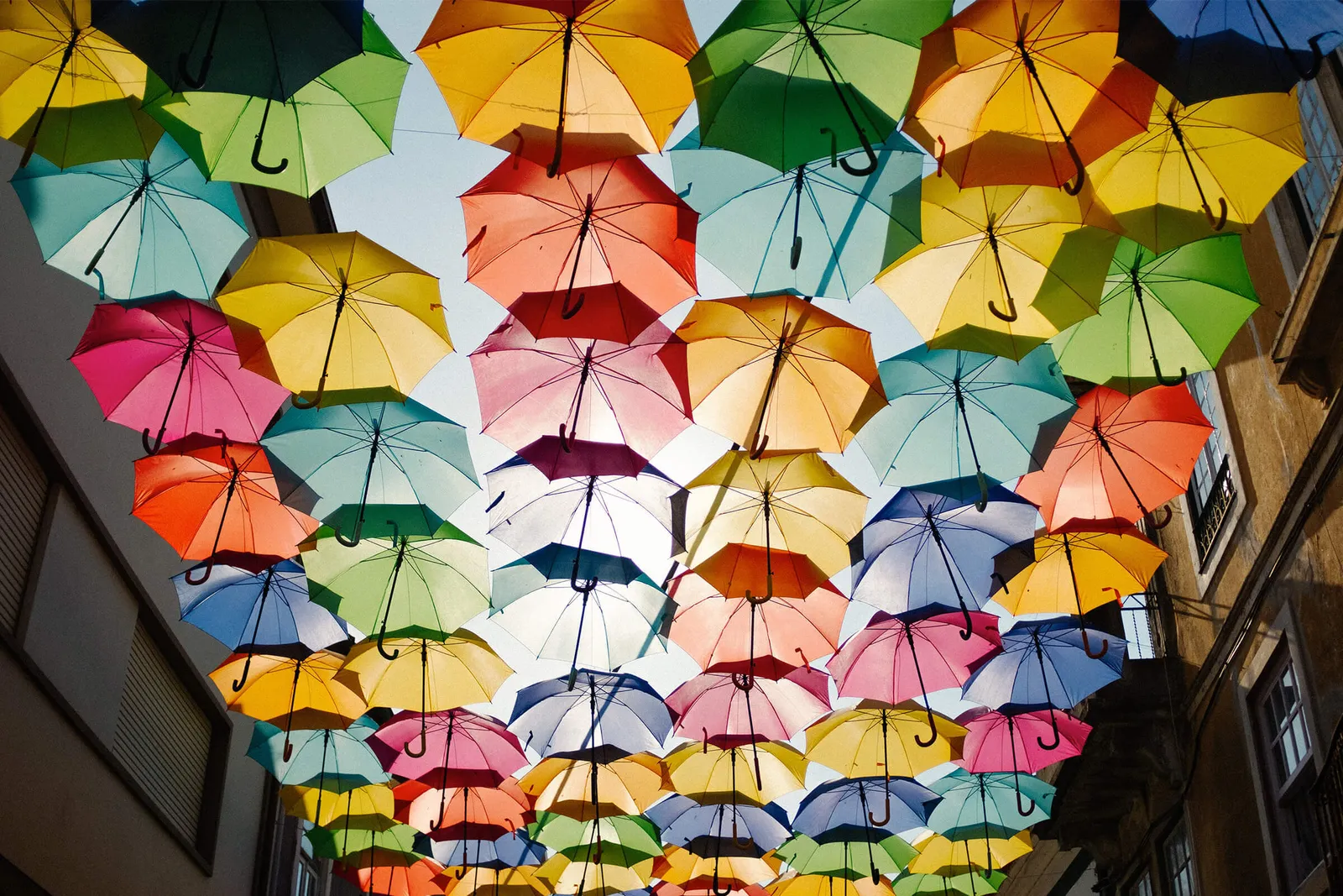 a collection of multi coloured umbrellas hung in between a street