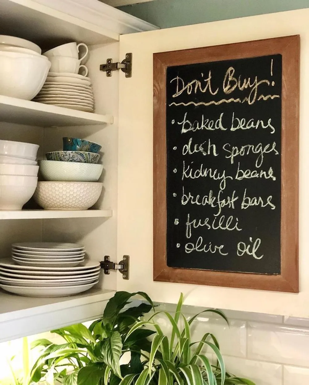 An open cupboard with a blackboard on it that reads "Don't buy: baked beans, dish sponges, kidney beans, breakfast bars, fusilli, olive oil"